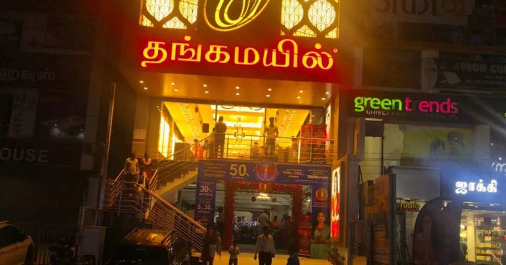 Front view of Thangamayil Jewellery Avadi showroom illuminated at night with bright signage and customers entering the store.